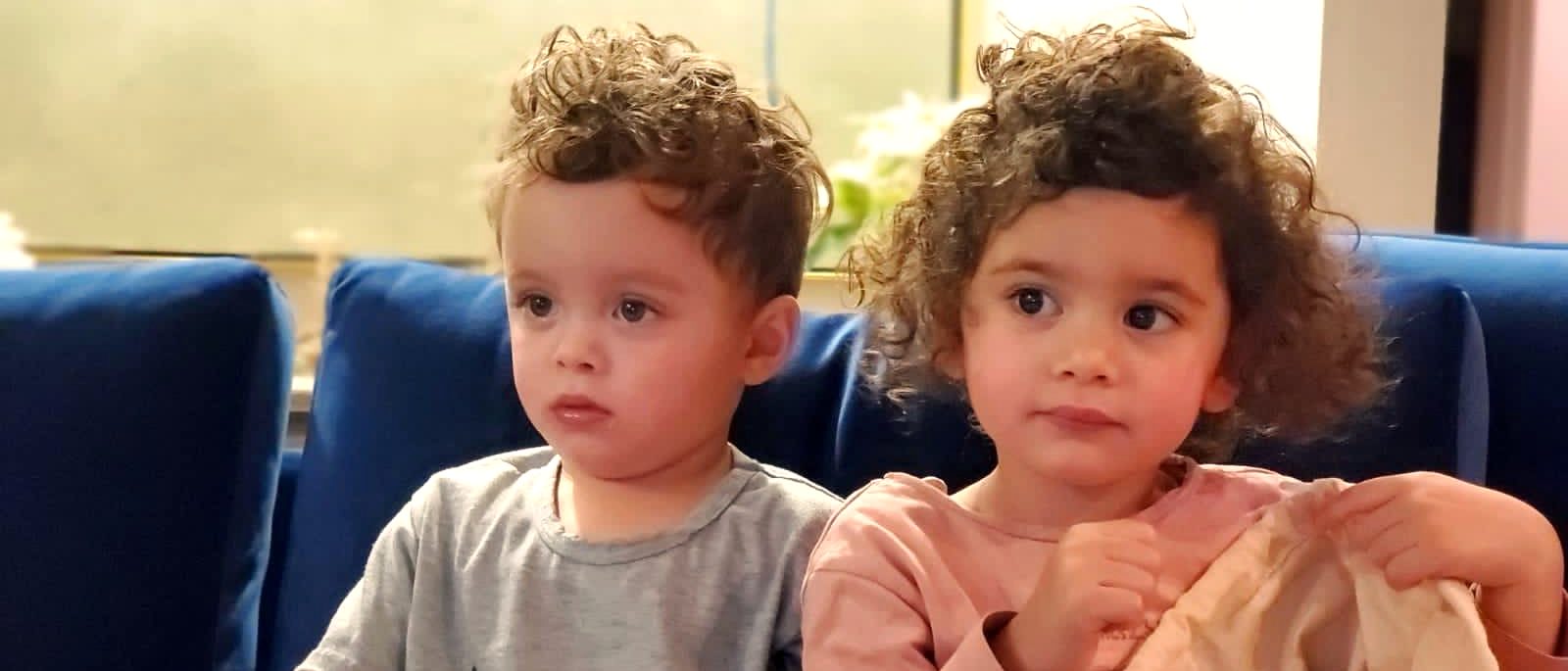 Two young children with curly hair sitting together on a blue sofa